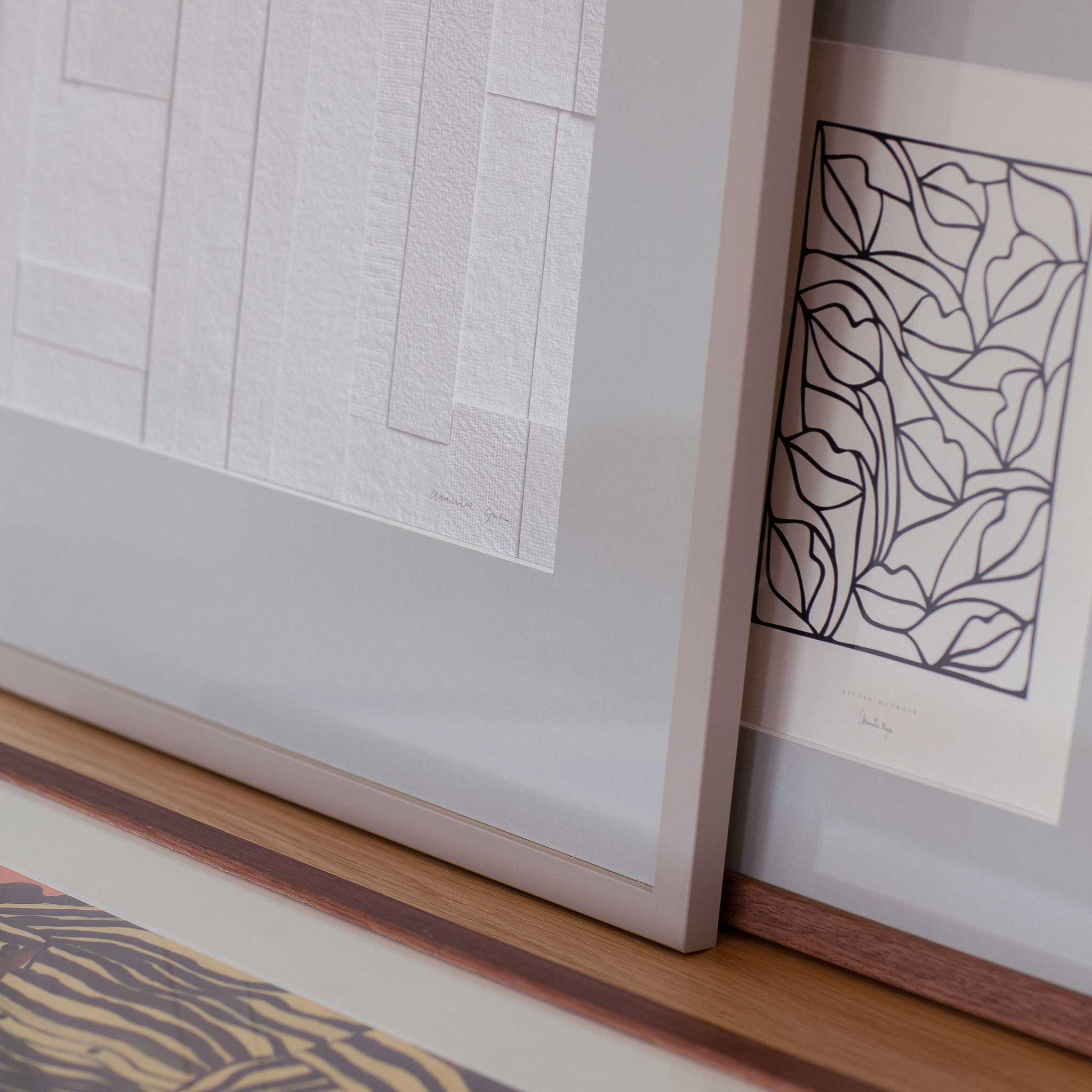 two framed artworks, one with a geometric design and the other with a floral pattern, displayed on a wooden surface.