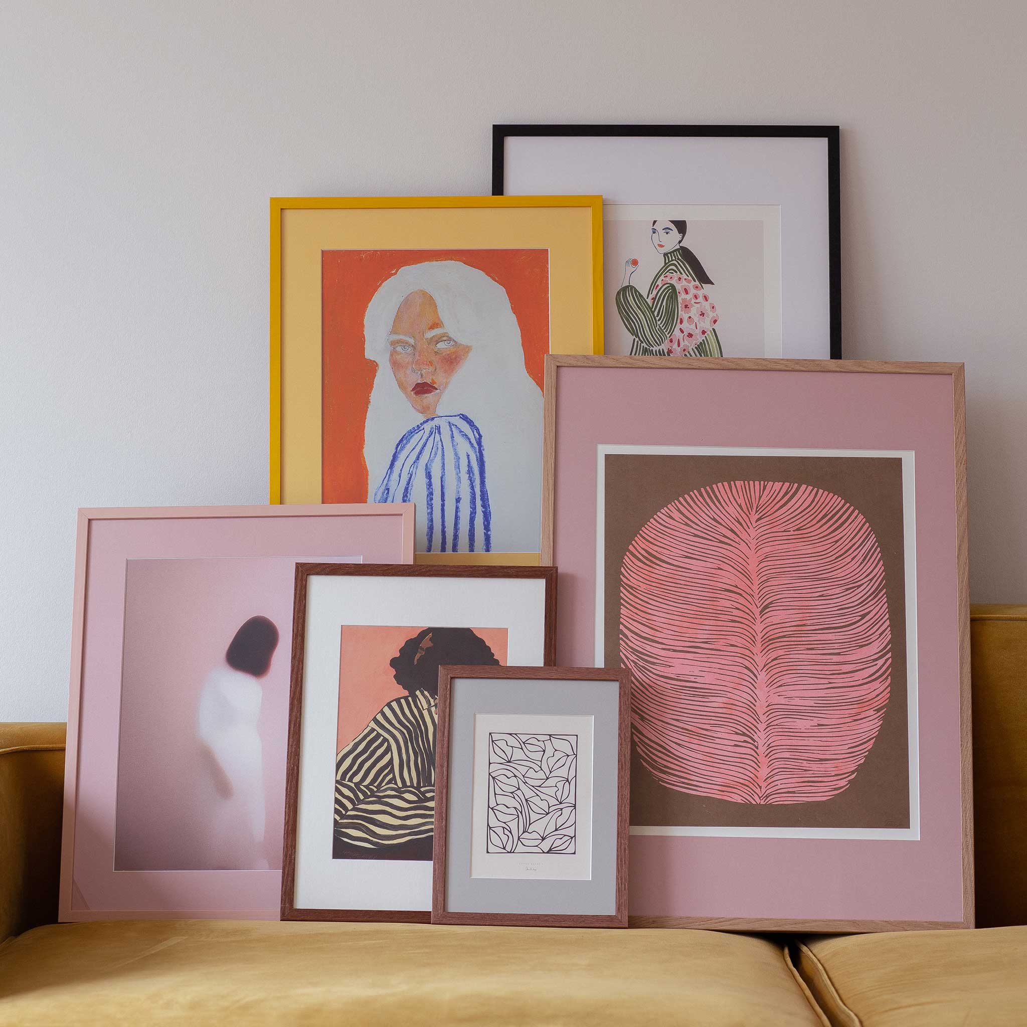 a collection of framed artworks, including a large pink frame with a pink leaf design, a framed portrait of a woman, and several other framed artworks with various styles and subjects.