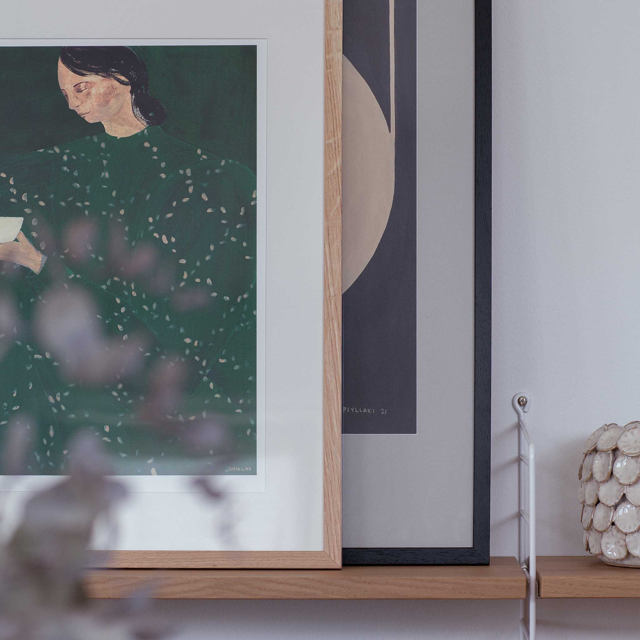a framed painting of a woman with a green dress, displayed on a wooden shelf.