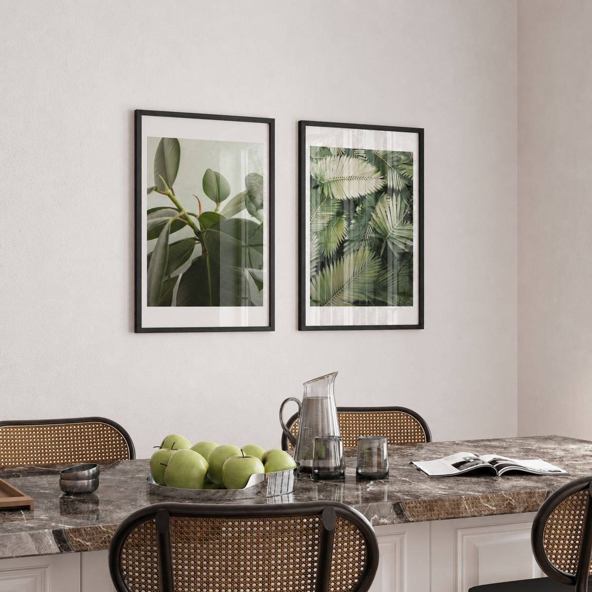 a dining room with a marble table and chairs, a bowl of green apples, and two framed prints of tropical plants hanging on the wall above the table.