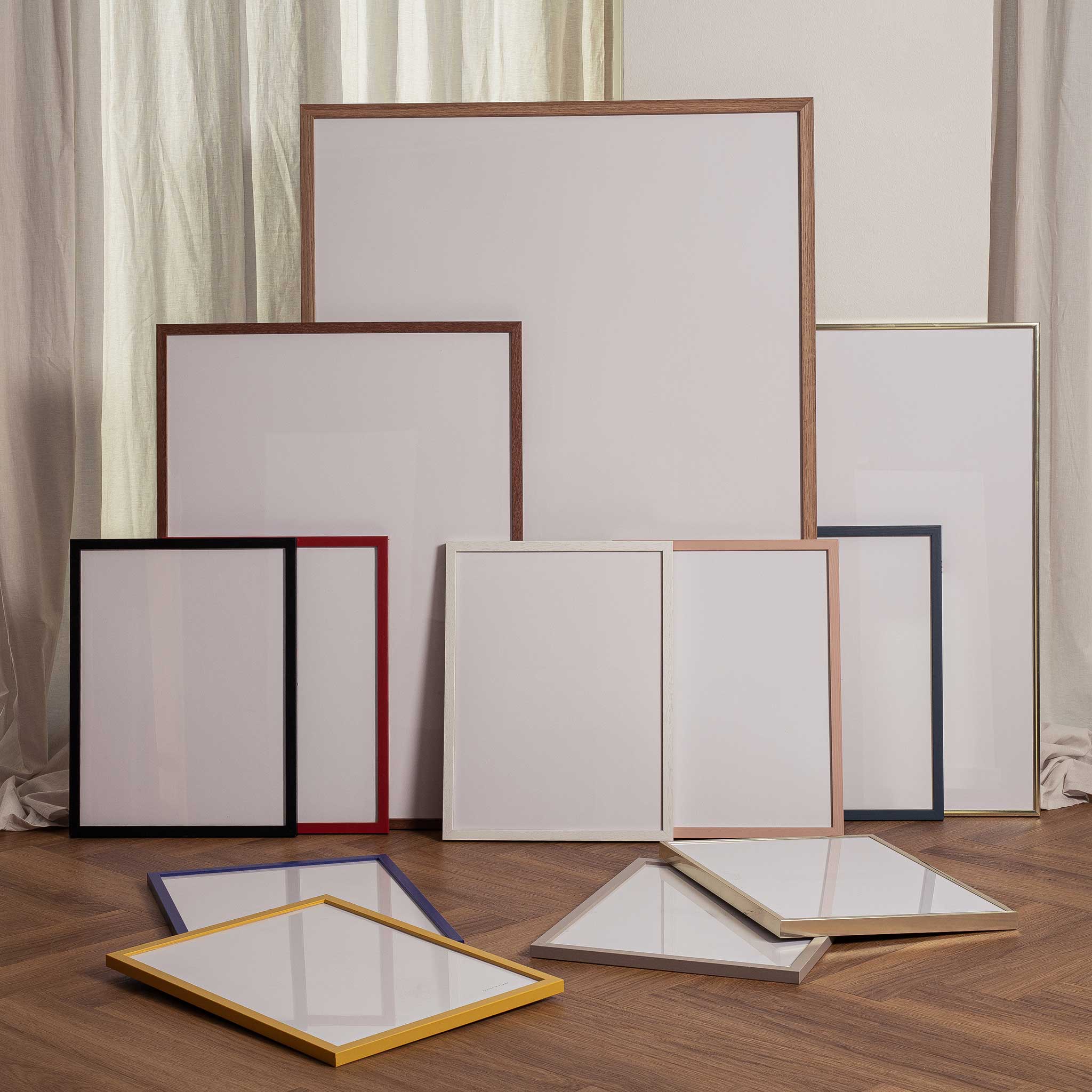 a collection of various-sized white picture frames arranged on a wooden floor.
