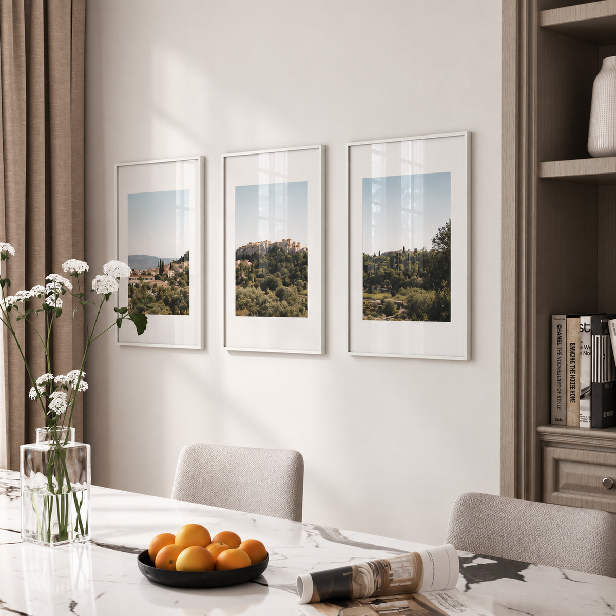 a dining room with a marble table, three framed landscape photographs hanging on the wall above it, and a vase of white flowers on the table.
