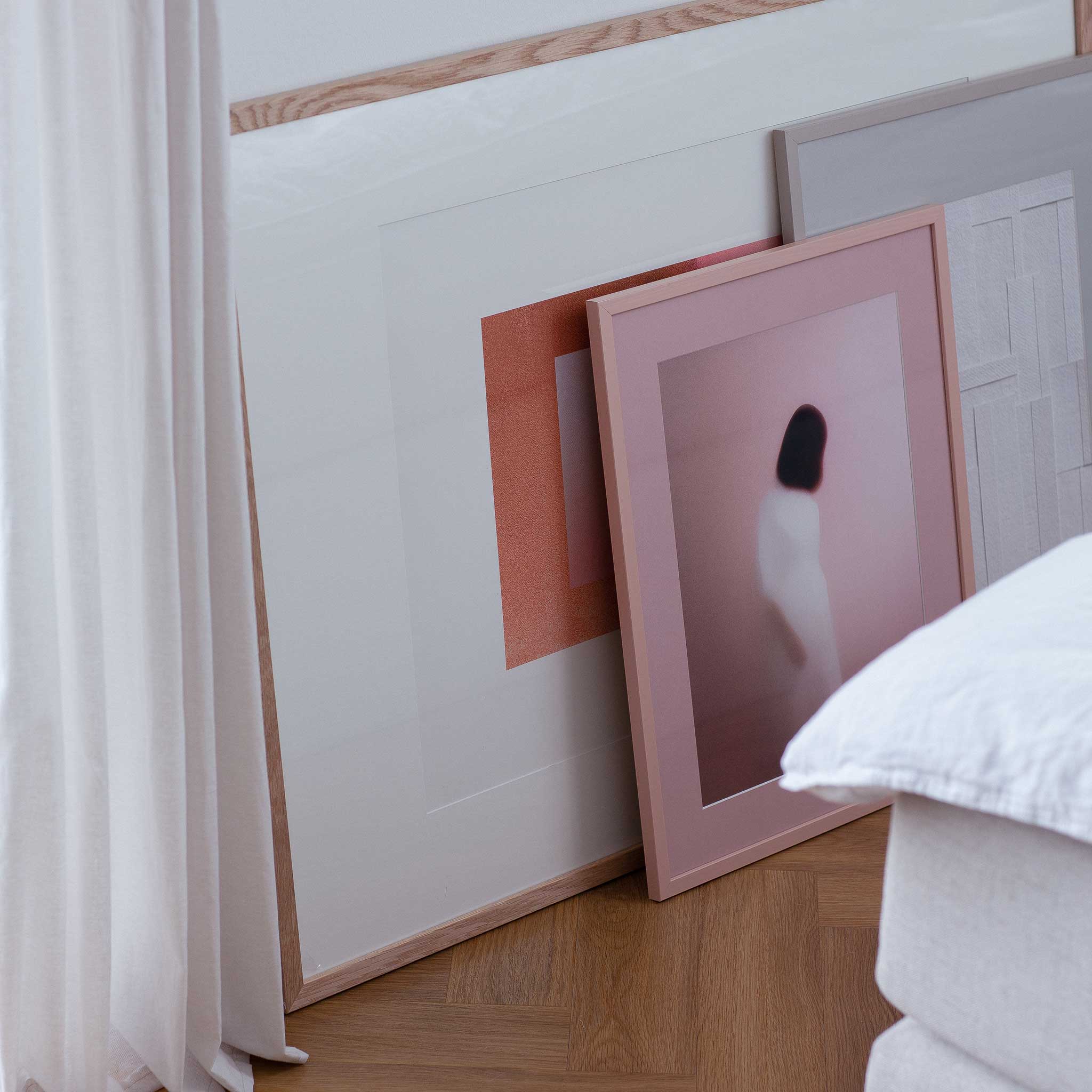 a collection of framed artworks displayed on a wall, with a pink frame prominently positioned in the foreground.