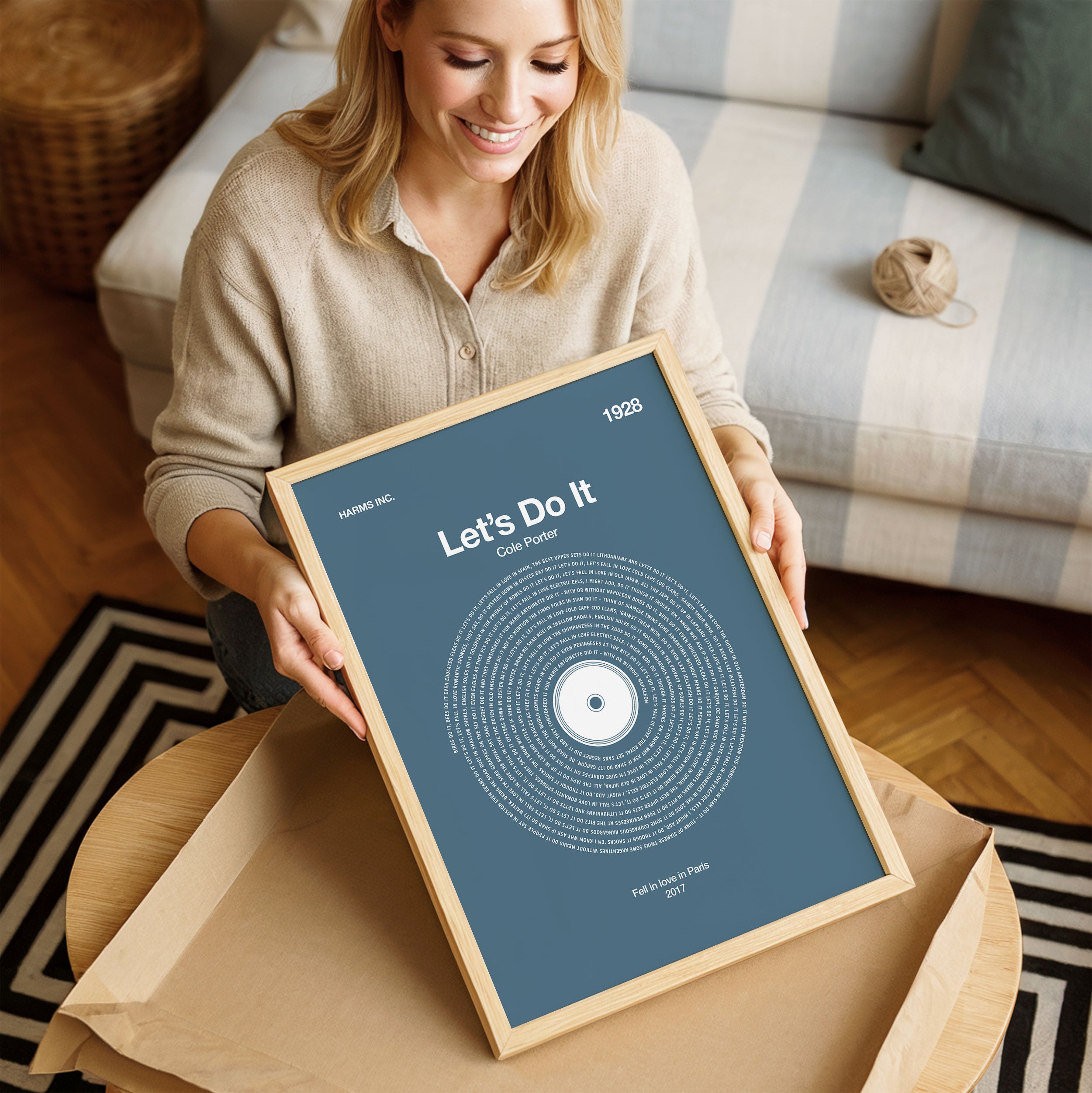 Soft Slate Blue background custom music wall art with personalized vinyl lyrics, contemporary aesthetic. Woman holding a framed poster with 'Let's Do It' text in a cozy living room.