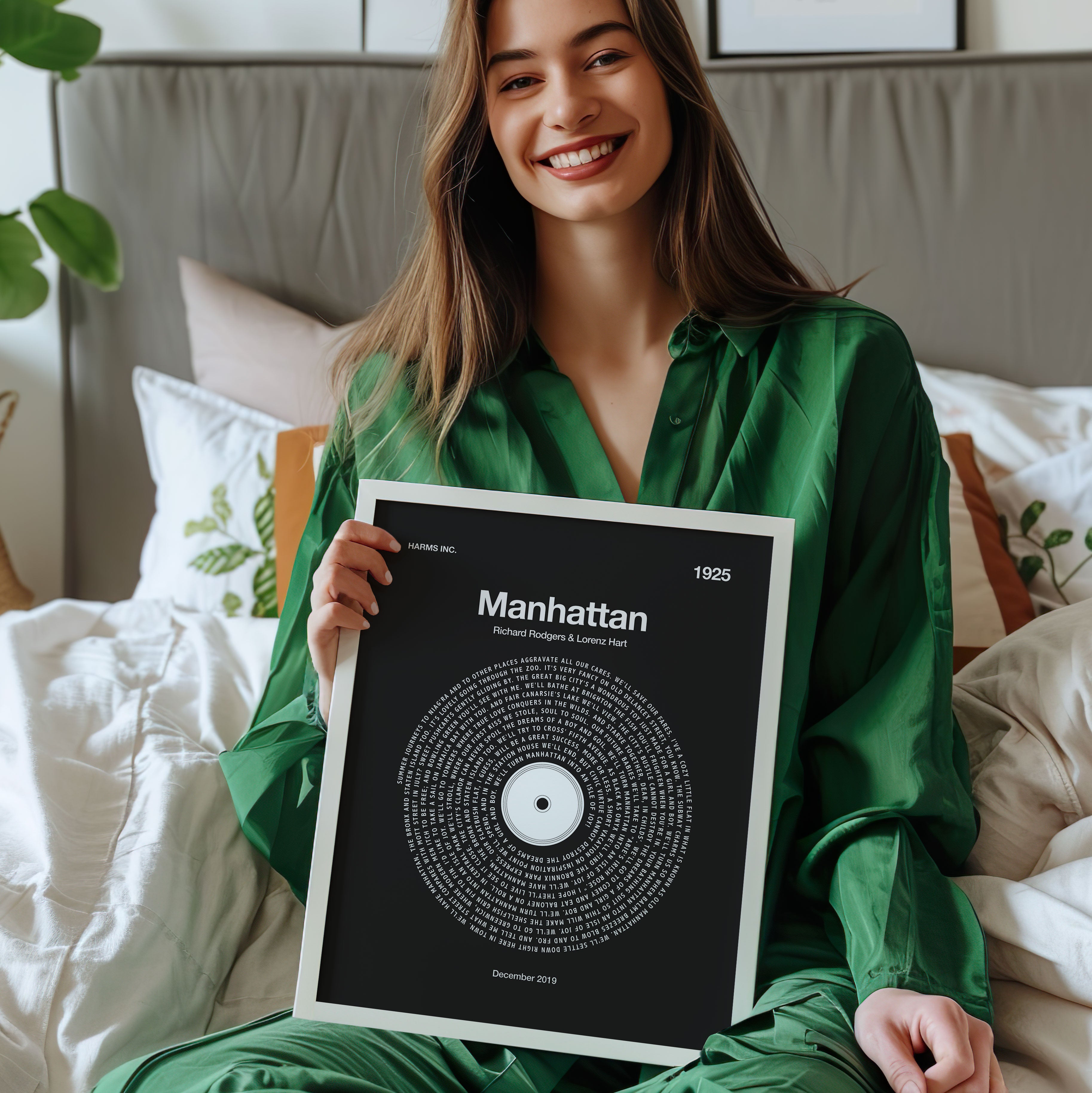 Charcoal background custom song lyrics print in a modern vinyl record style. Woman holding a framed artwork titled 'Manhattan' in a bedroom setting.