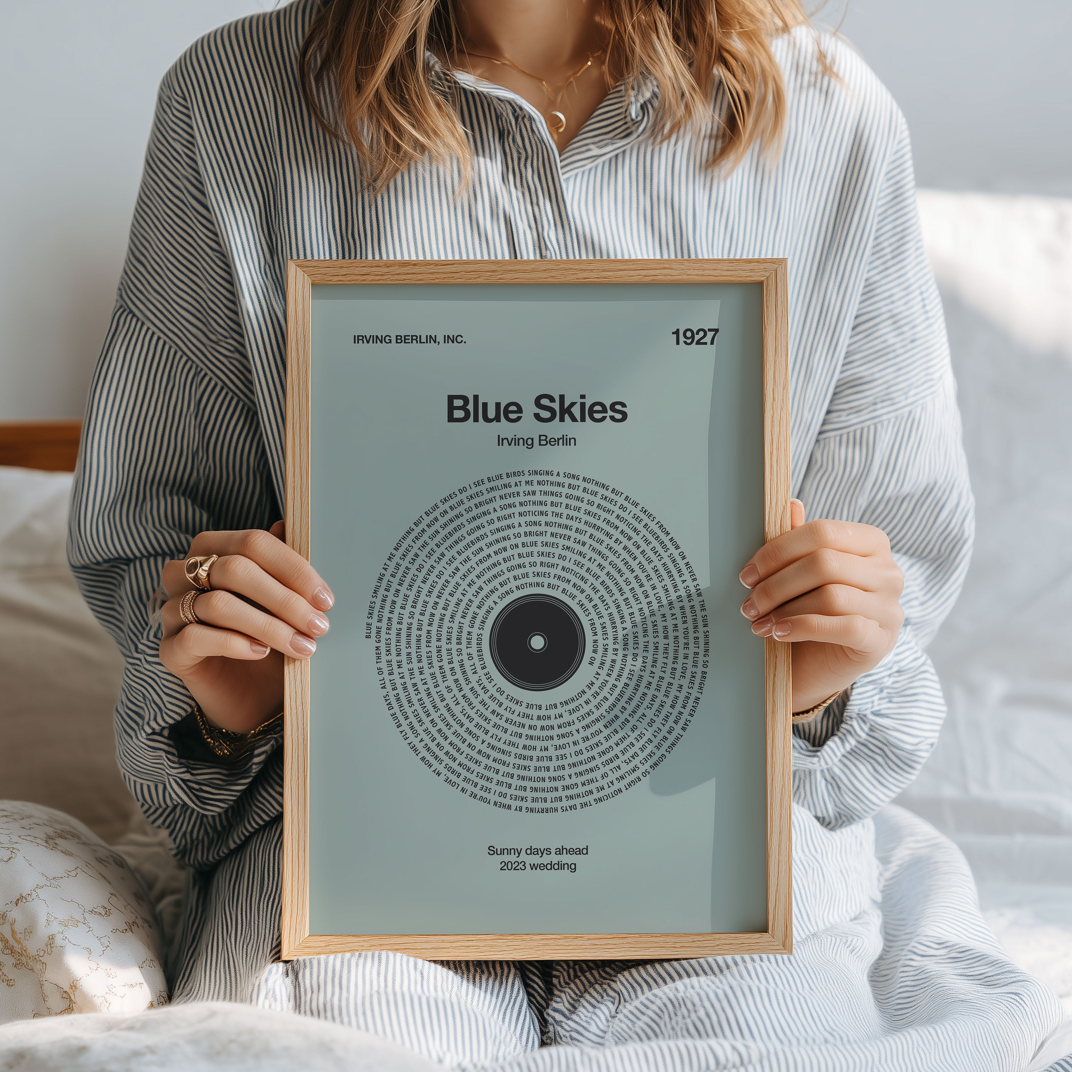 Soft Sage background custom lyrics wall art in a vinyl record design, heartfelt personalized music print. Person holding a framed print titled 'Blue Skies' by Irving Berlin.