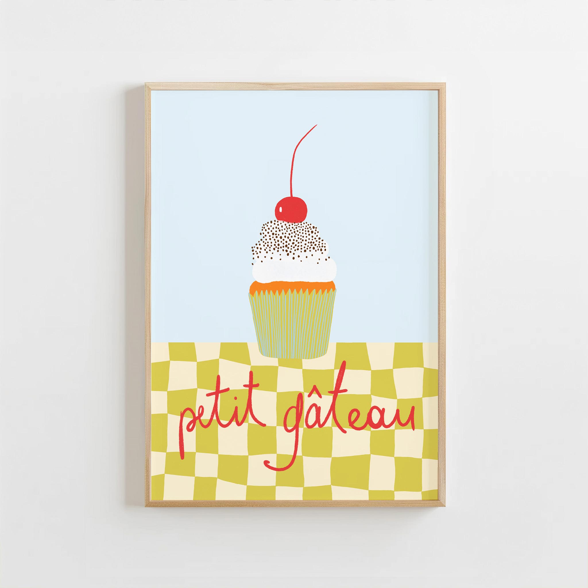 Framed artwork of a cupcake with a cherry on top and 'petit gateau' text on a checkered background.