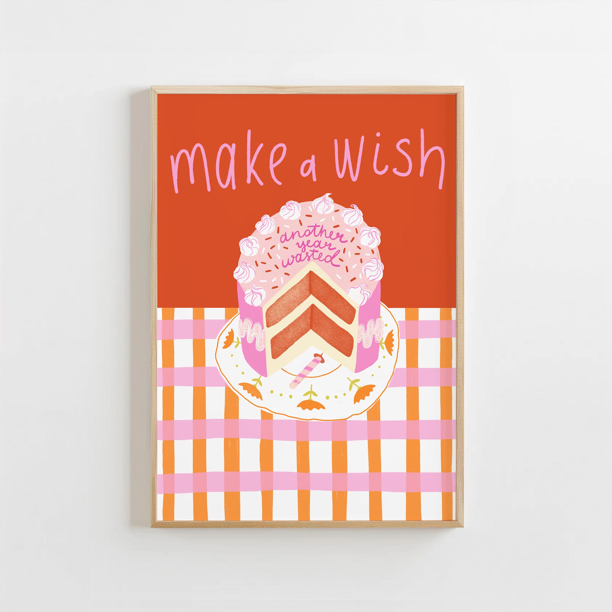 Framed artwork with a cake illustration and 'make a wish' text on an orange background.
