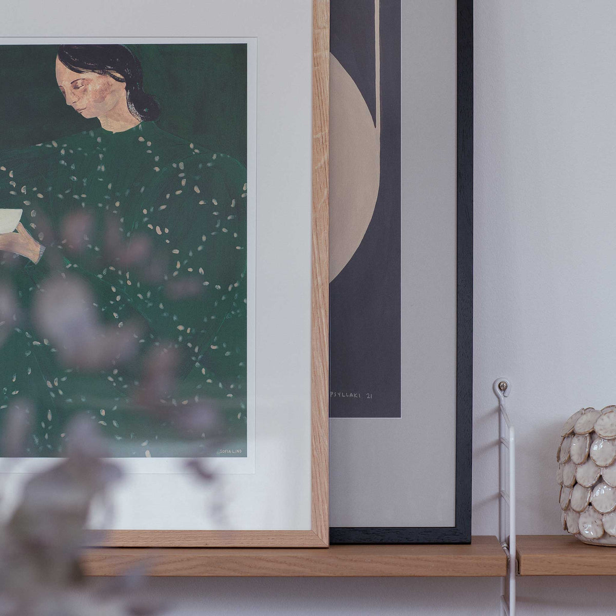 a framed painting of a woman with a green dress, displayed on a wooden shelf.